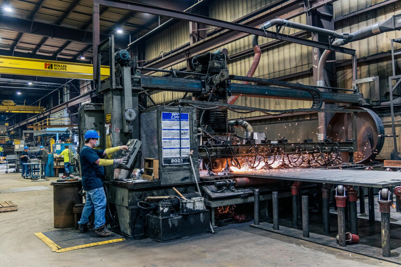 A worker wearing safety gear operates machinery in a busy manufacturing factory.